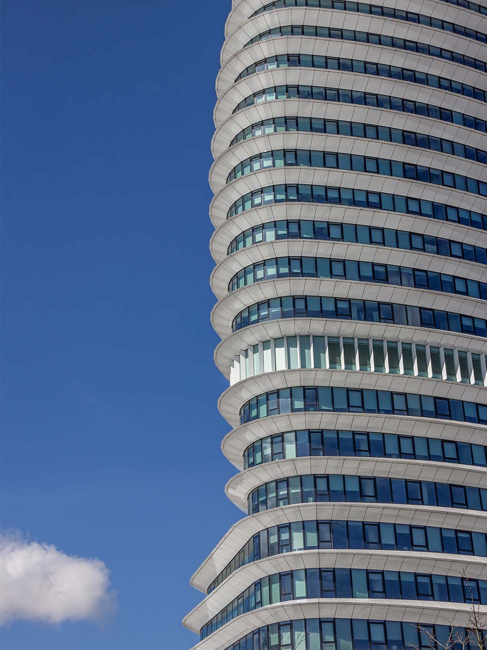 Hoog kantoorgebouw met gebogen gevel, glazen ramen en witte gevelpanelen tegen een strakblauwe lucht, geschikt voor kantoorvastgoed en zakelijke locaties.