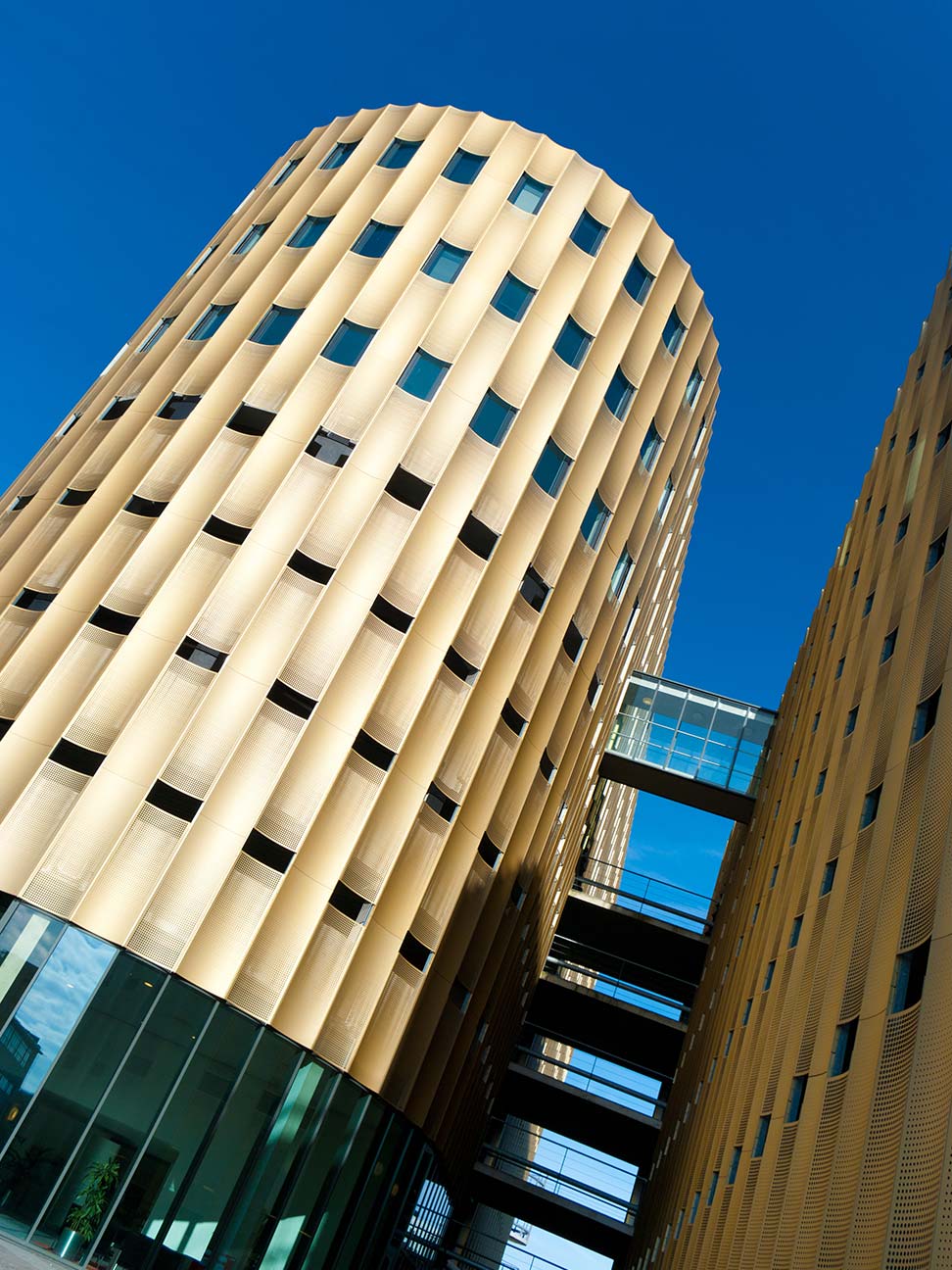 Kantoorgebouw in Zwolle met goudkleurige gevel, verticale architectonische lijnen en glazen luchtbruggen tussen twee torens, passend bij kantoorruimte en huurprijs per vierkante meter.