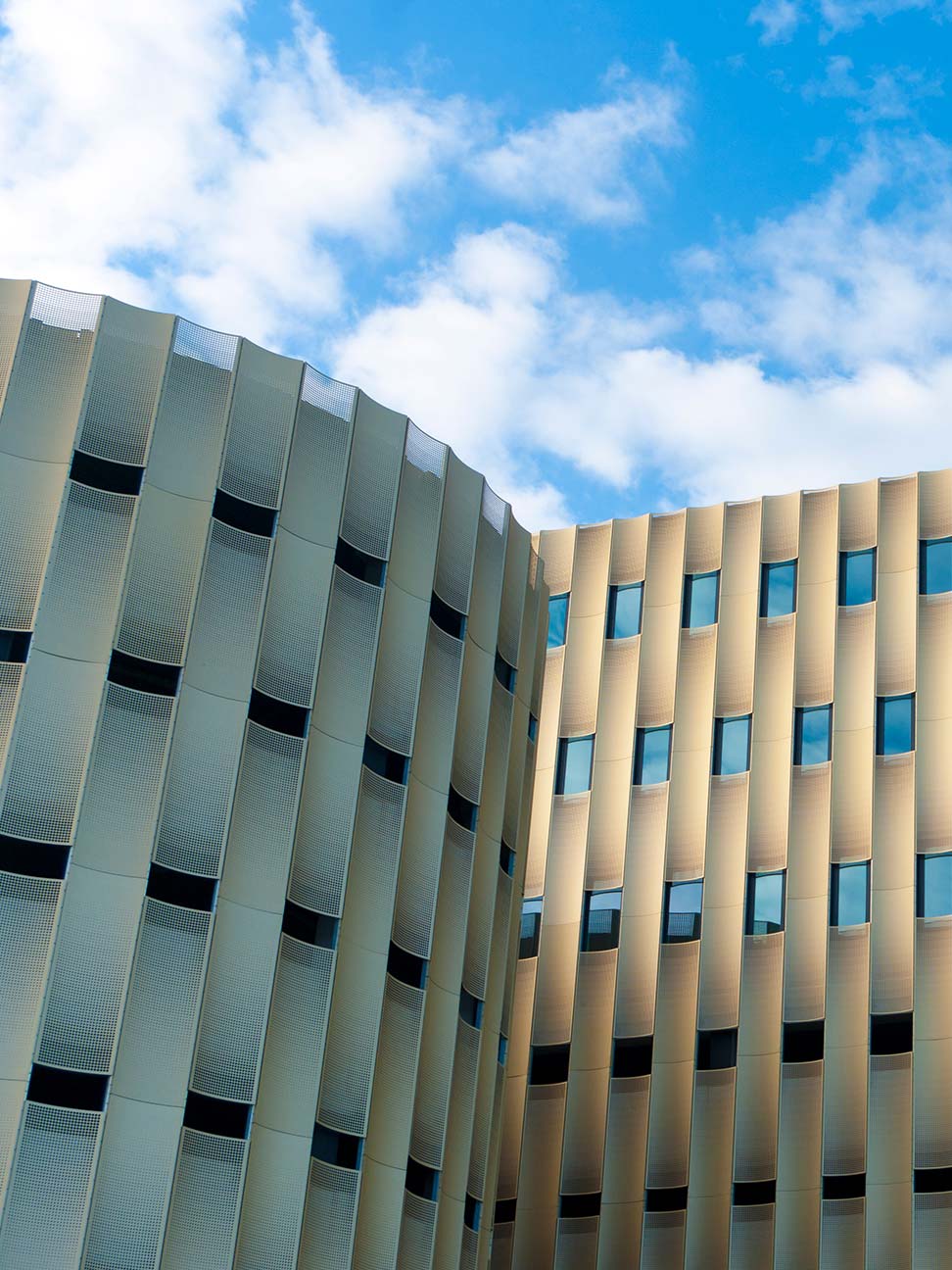 Kantoorgebouw in Zwolle met goudkleurige gevel, verticale architectuur en smalle ramen onder een blauwe lucht met wolken.