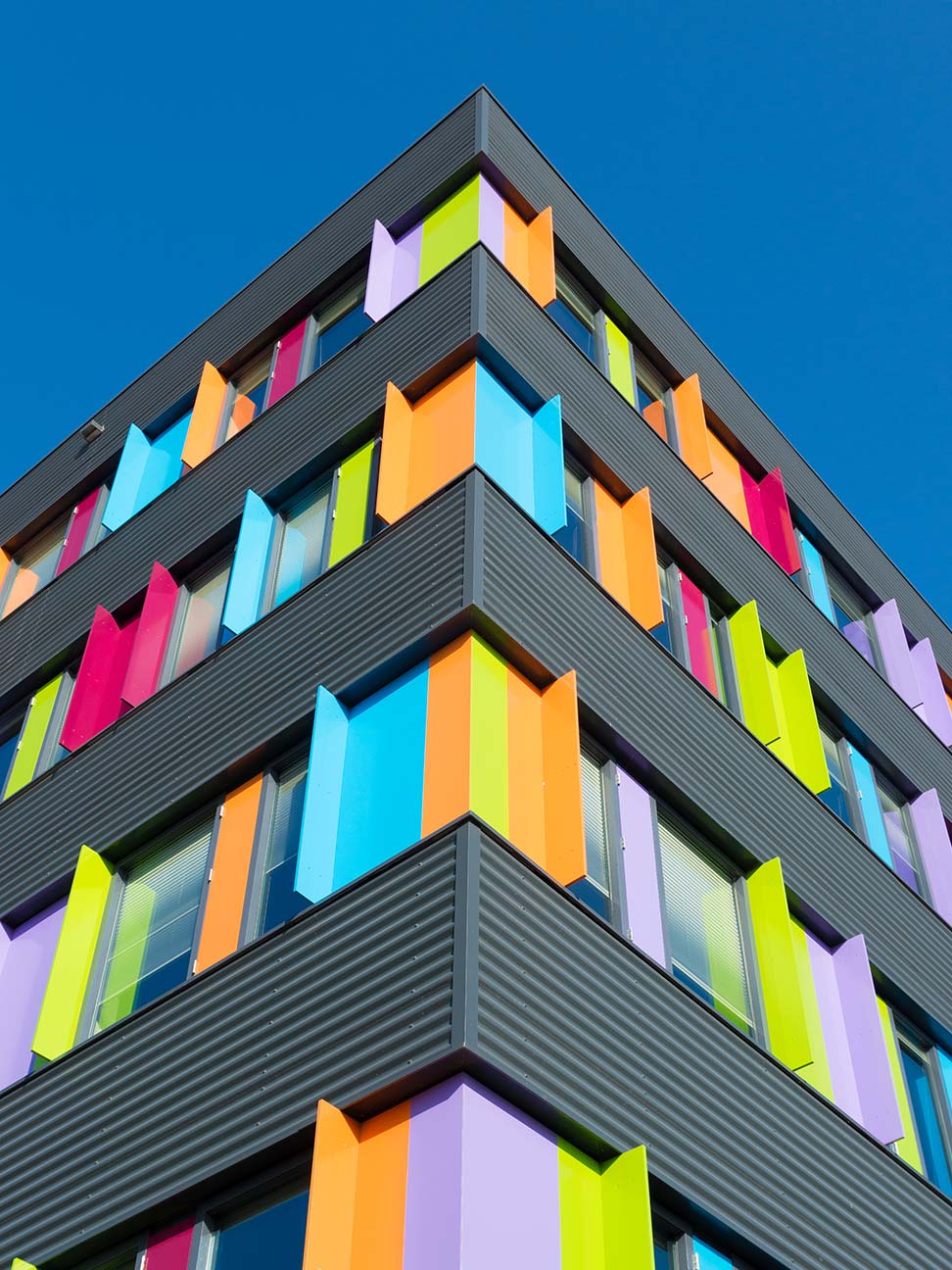 Kantoorruimte in Zwolle met kleurrijke gevelpanelen, grote ramen en opvallende architectuur tegen een heldere blauwe lucht. Geschikt voor zakelijke huisvesting en kantoorverhuur.