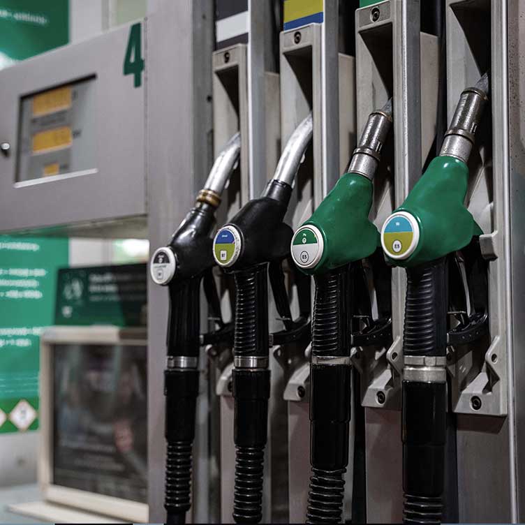 Close-up of four fuel nozzles at a petrol station, each colour-coded and labelled for different types of fuel.