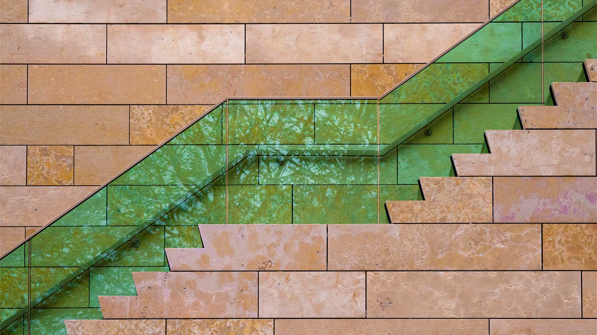 Moderne stenen muur met diagonale groene glazen trap en reflectie van bomen, architectonische gevel met strak geometrisch design.
