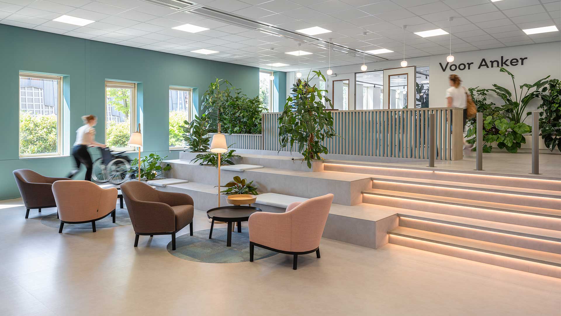Modern entrance hall or waiting area with light blue walls, comfortable seating, illuminated stairs, and green plants. Ideal for healthcare facilities, office environments, and public spaces, focusing on accessibility and inviting design.