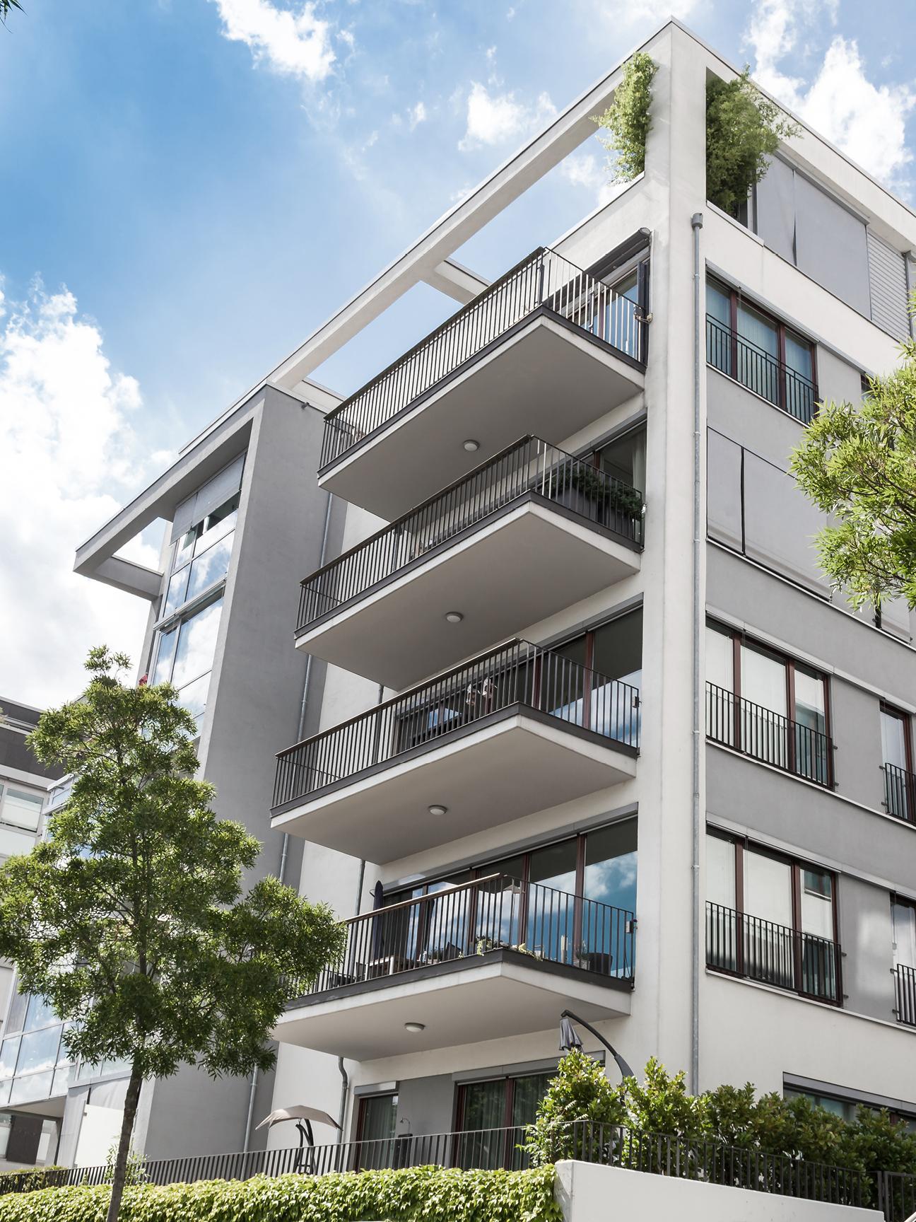 An apartment complex with six floors, spacious balconies and surrounded by what appears to be a green living environment.