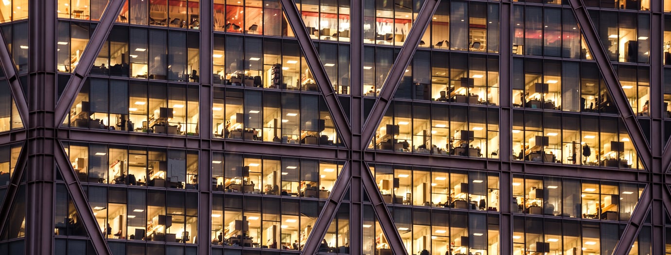 Facade of a London office tower at dusk, with lit floors visible behind its diagonal steel frame.