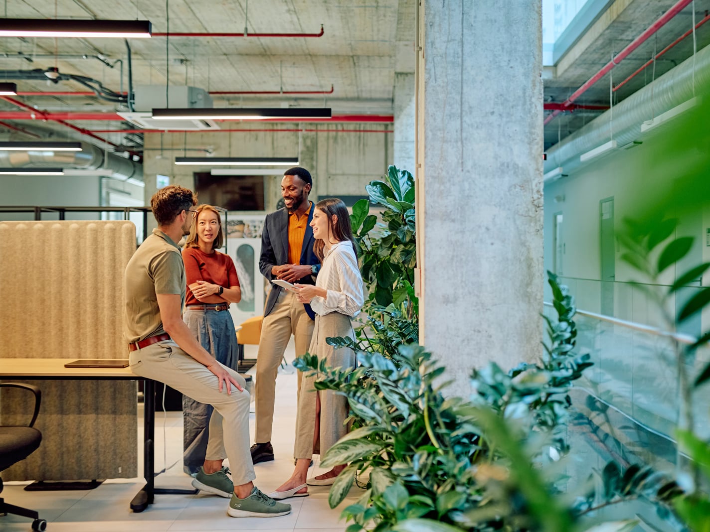 Group of diverse businesspeople engaged in a project discussion within a modern shared and private office filled with lush plants, fostering collaboration and creativity