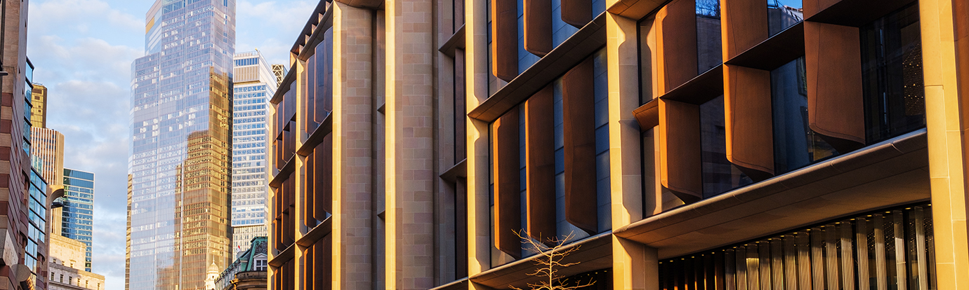 A low-angle shot of a modern urban building with distinctive bronzed fins in London, set against a backdrop of glass skyscrapers and a clear sky.