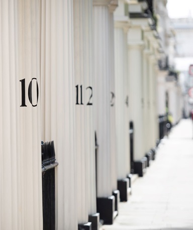 A row of white townhouses with a shallow depth of field focusing on the house numbers "10" and "11", with other blurred numbers in the background
