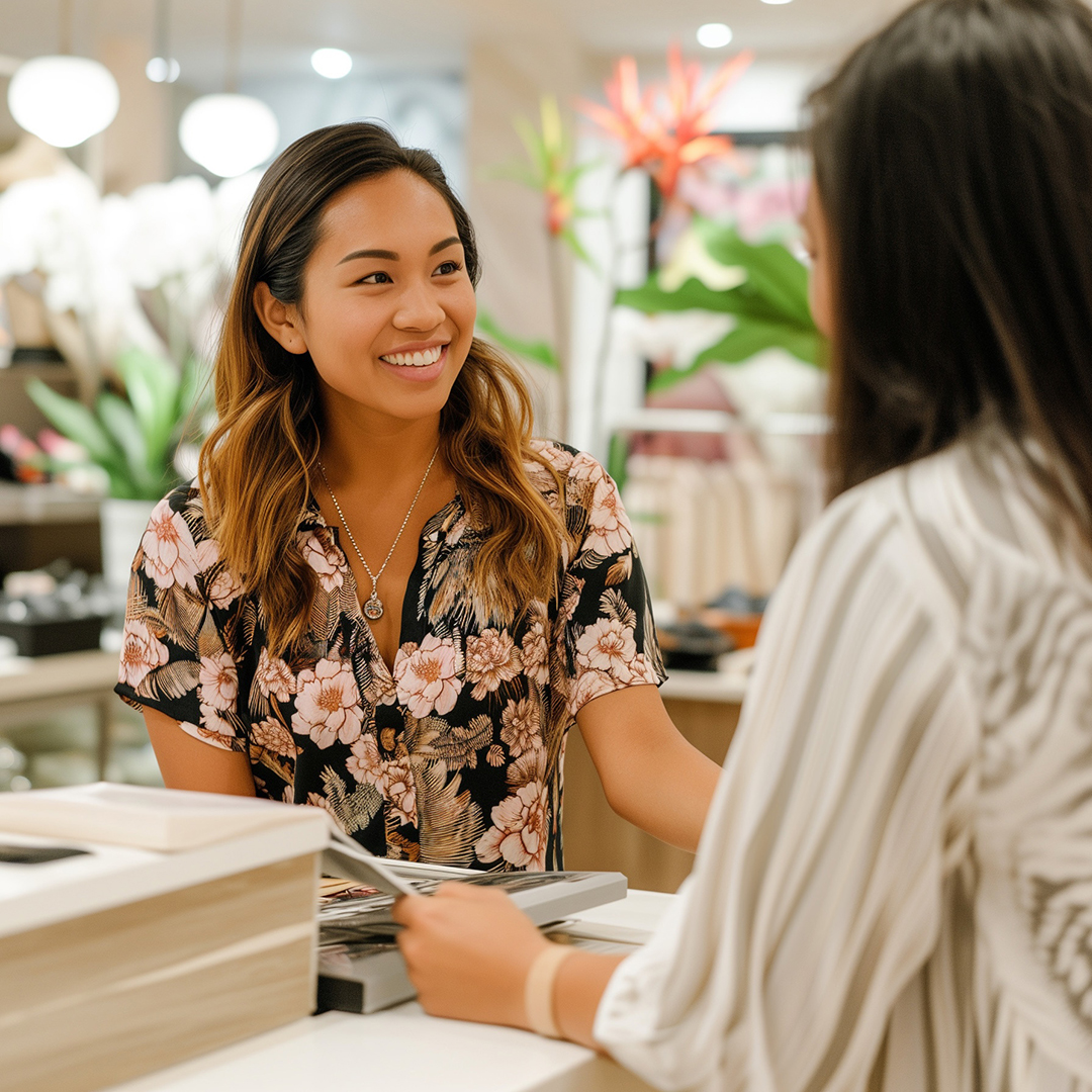 Smiling retail store associate in a floral top assisting a customer at the checkout counter inside a boutique with tropical decor in Hawaii.