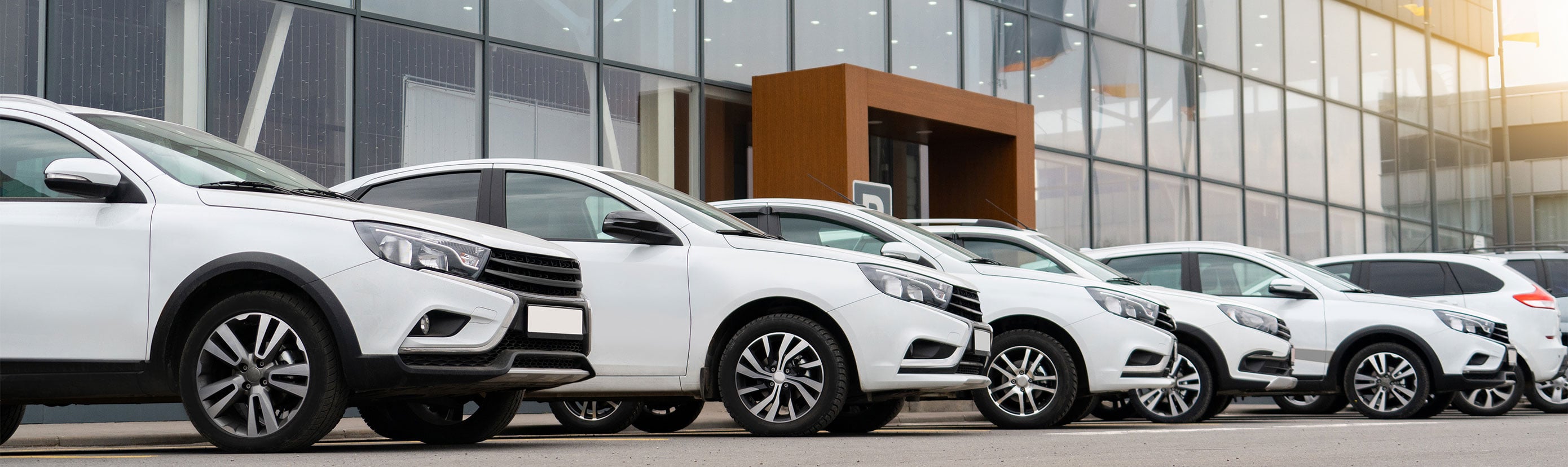 Row of new vehicles parked in front of a modern auto dealership with glass facade