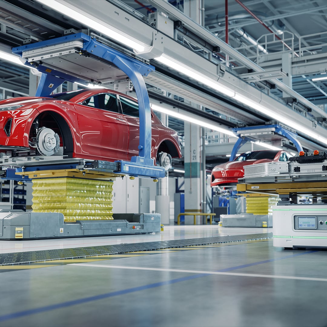 Red electric vehicle body being assembled on an automated automotive production line with robotic equipment and conveyor systems in a modern factory.
