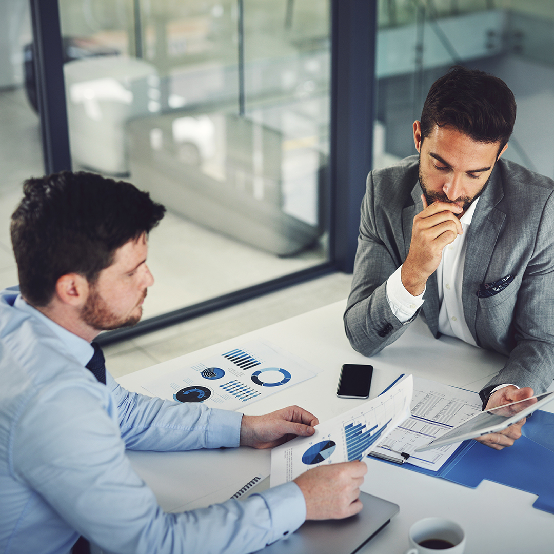 Two professionals reviewing business charts and graphs in modern office setting