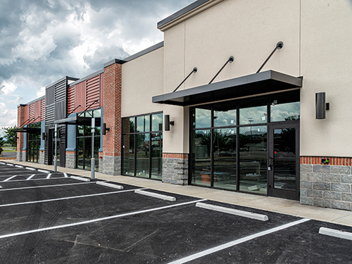 Modern strip mall storefront with black awnings and empty parking spaces under cloudy sky