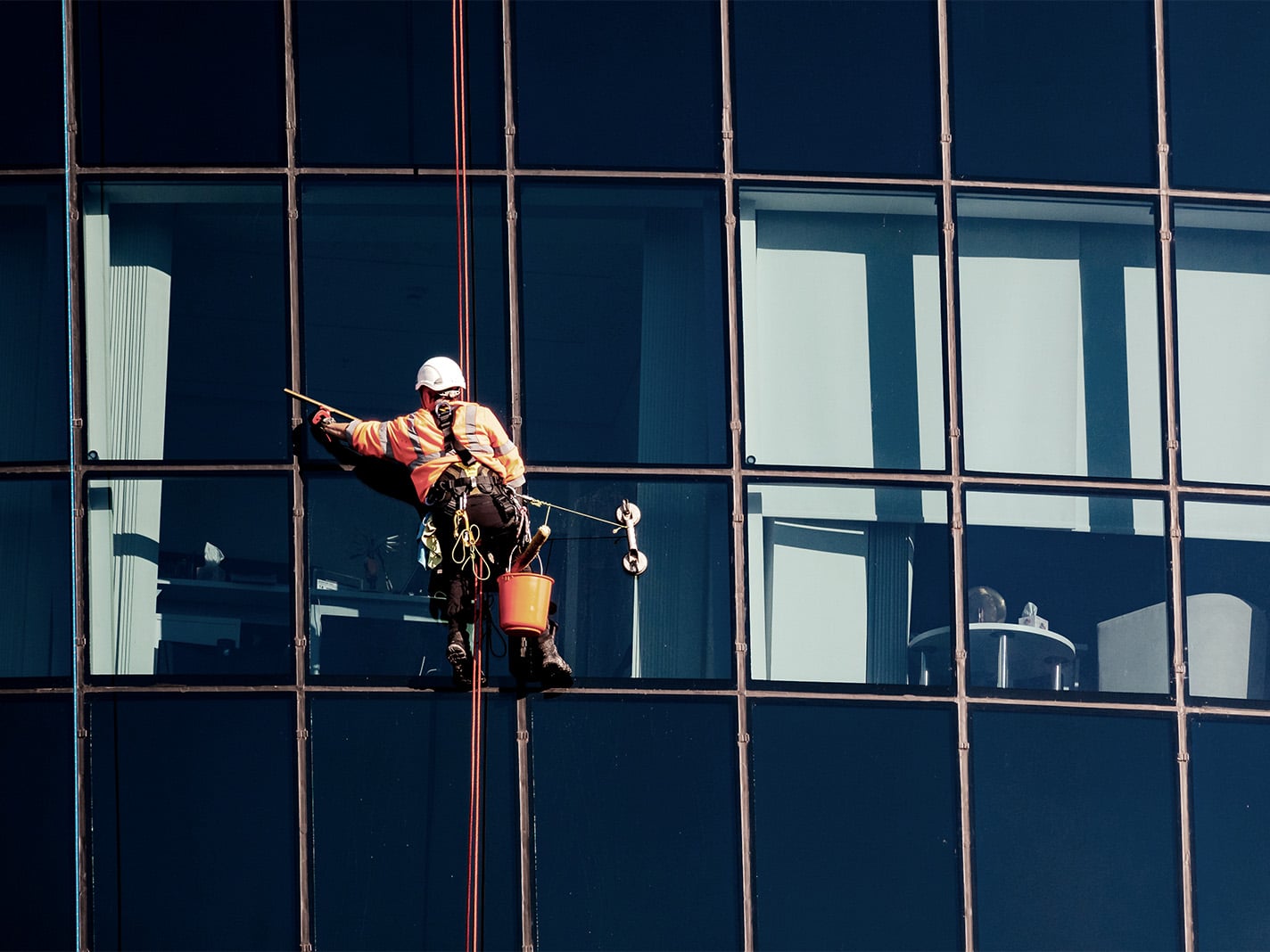 Rope access technician in safety gear cleaning the glass curtain wall of a commercial office building
