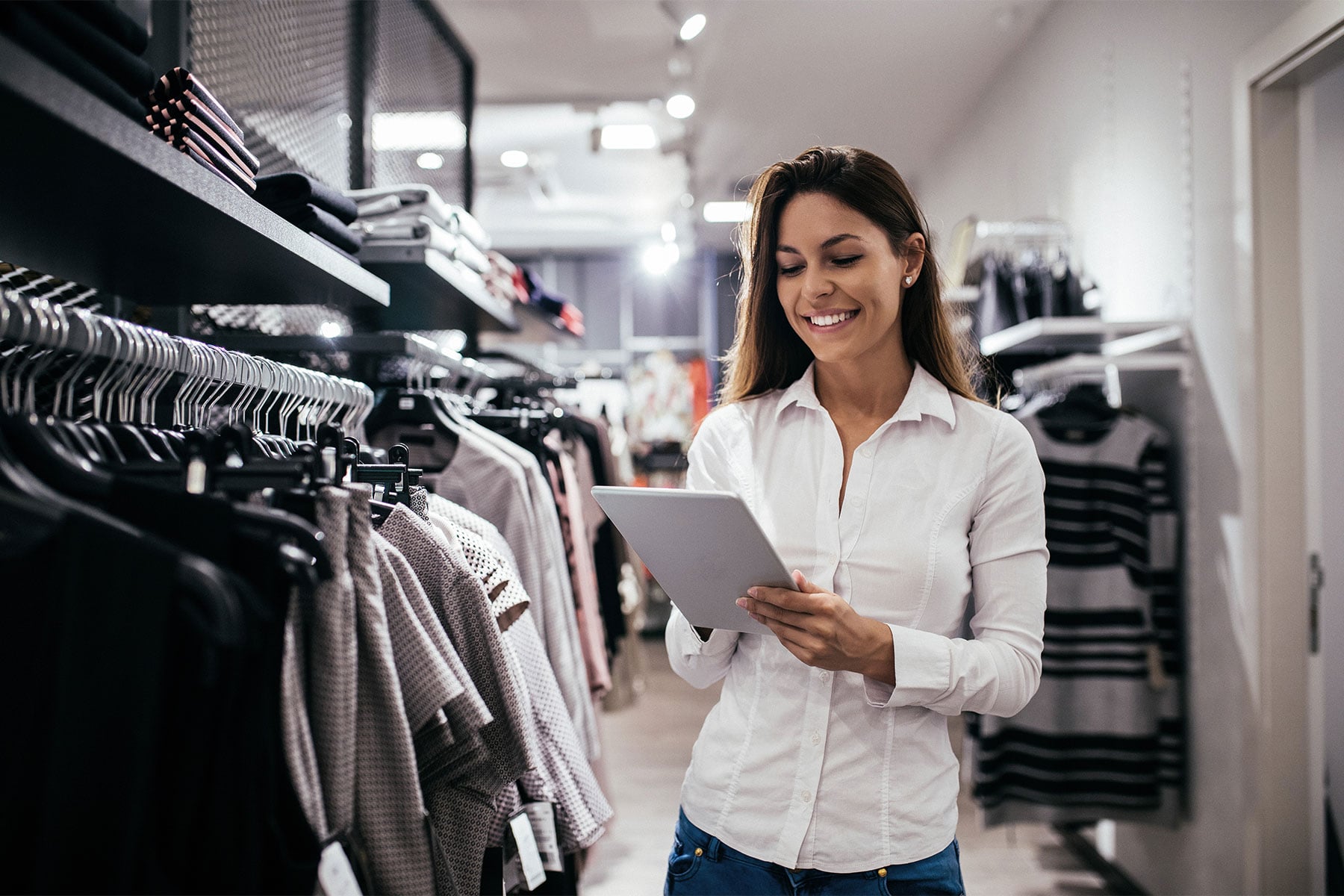 Person using a digital tablet to manage inventory in a modern clothing retail store.