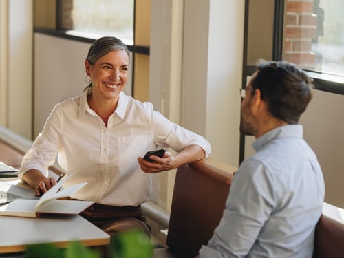 Two colleagues having a conversation at a bright office workspace near a window