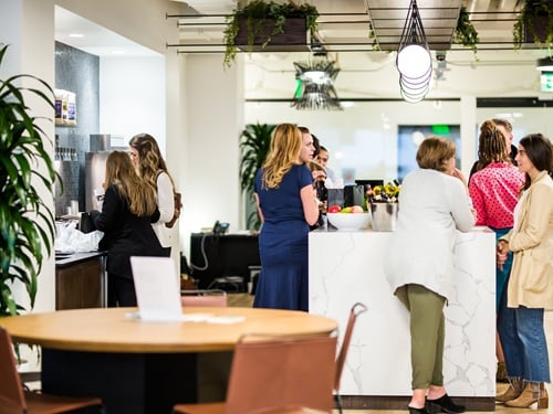 Professionals networking in a modern workplace amenity space with a reception counter and lounge seating