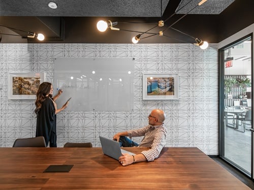 Two professionals collaborating in a contemporary conference room with a whiteboard and wood table