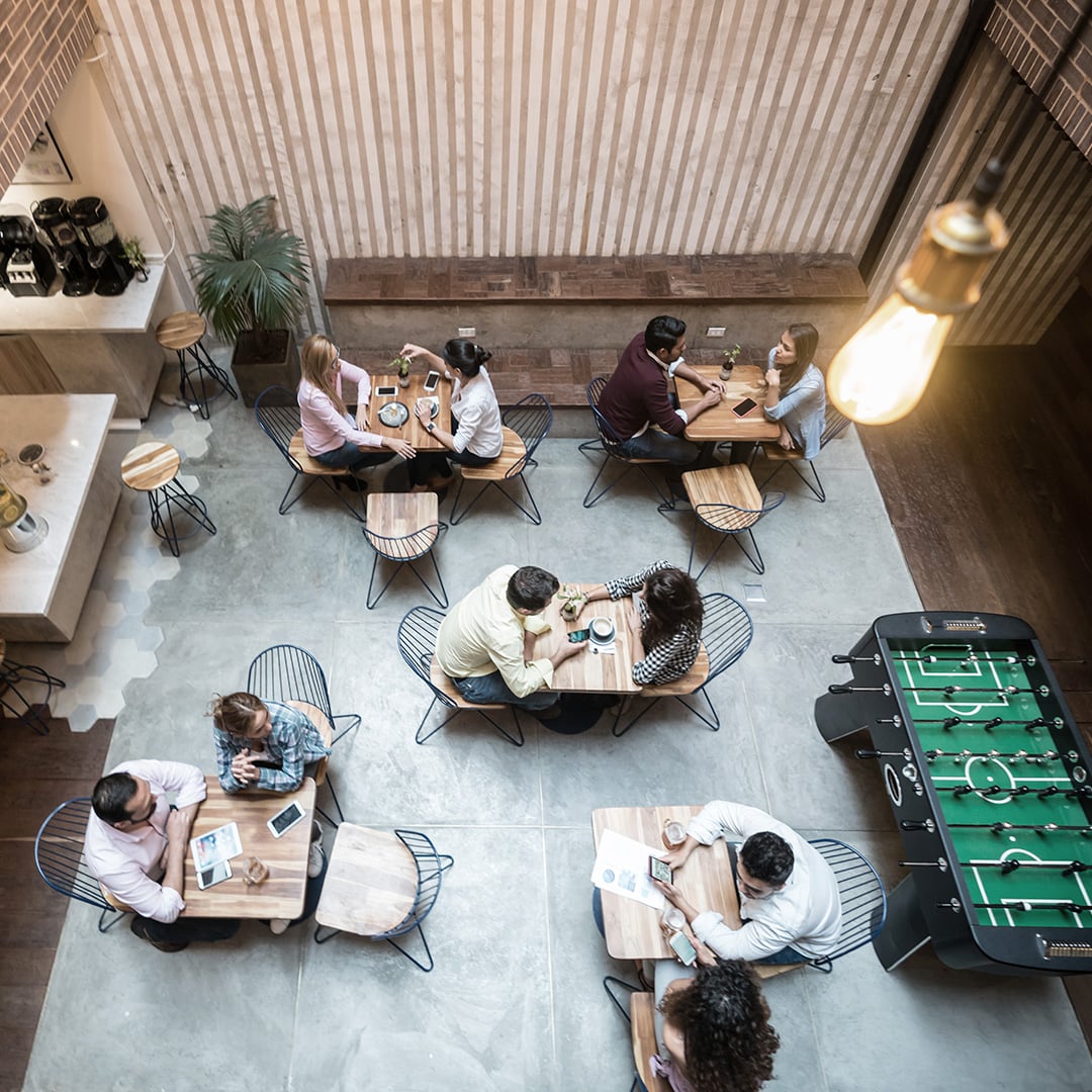 Aerial view of employees collaborating at tables in a modern office breakroom with a foosball table, illustrating CBRE's organizational change management and workplace transformation services.