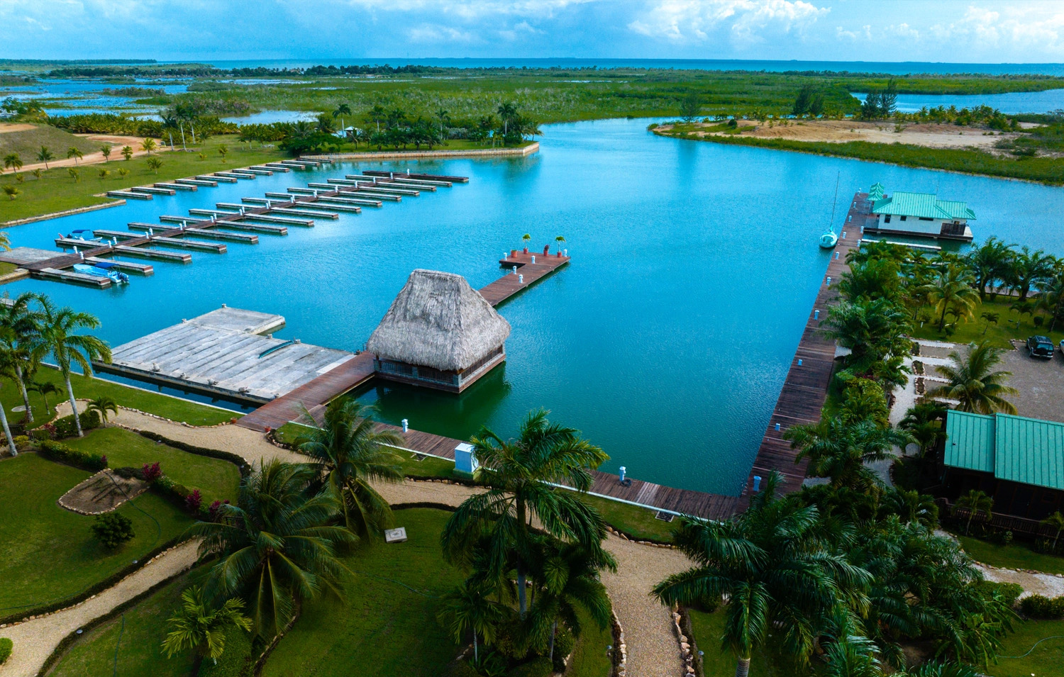 Aerial view of a tropical marina with wooden boat docks, turquoise water, palm trees, and surrounding coastal landscape