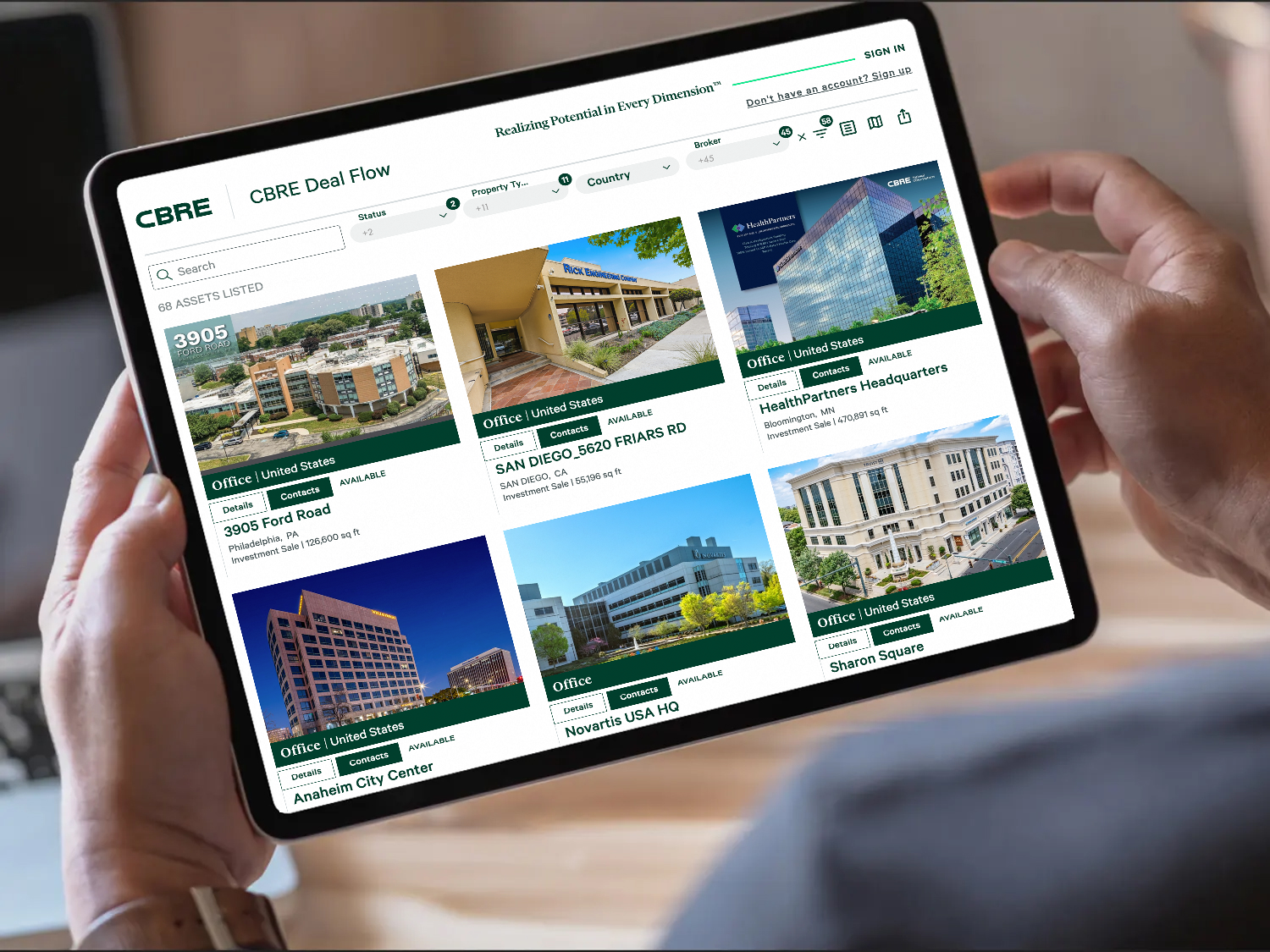 A person holding a tablet displaying various commercial real estate listings from CBRE, including images and brief descriptions of properties such as office buildings, development sites, and mixed-use complexes.