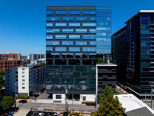 Aerial exterior of The Moore Building, a modern dark glass and black metal panel mid-rise office tower with distinctive grid curtainwall facade in an urban setting.