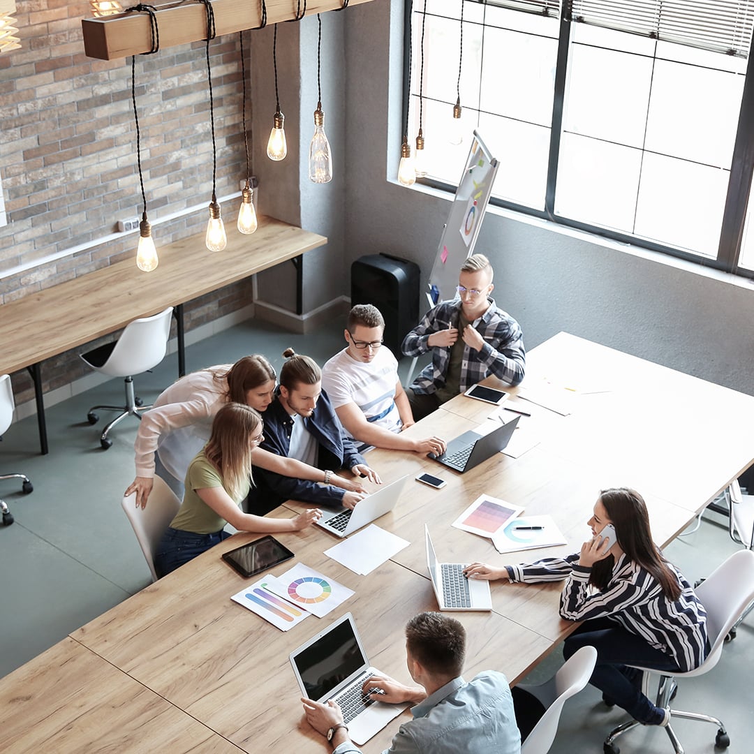 Team of professionals collaborating around laptops and data charts in a modern office, representing CBRE Labor Analytics workforce and location strategy consulting.