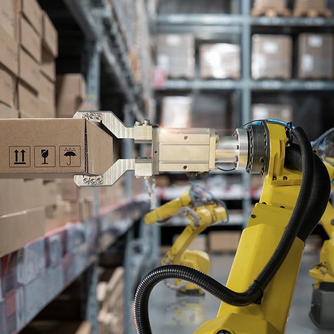 Yellow robotic arms autonomously handling cardboard boxes on warehouse shelving in a modern automated fulfillment center