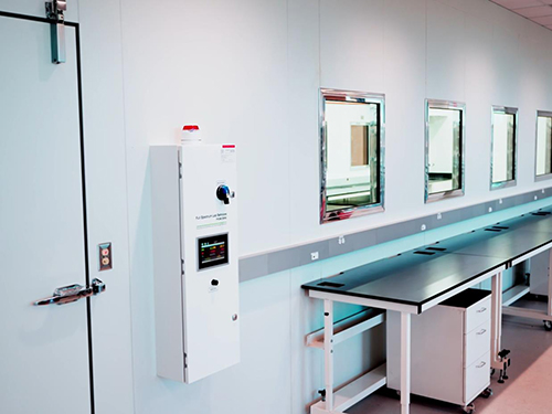 Cleanroom corridor with environmental monitoring control panel labeled Full Spectrum Lab Services from CBRE alongside a stainless lab bench.
