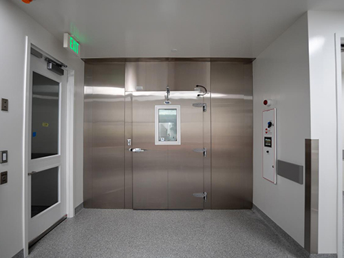 Stainless steel insulated cold room door in a biotech facility vestibule with adjacent lab entry and emergency alarm panel, part of CBRE life sciences operations.