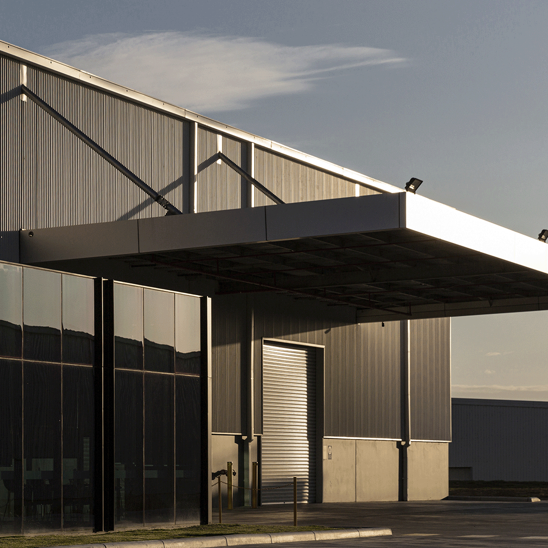 A modern industrial building with a large roller door, glass facade, and a prominent canopy extending from the roof.