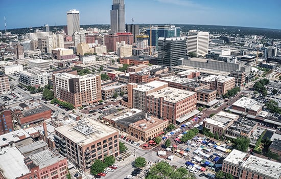 Aerial view of Omaha downtown skyline with historic Old Market district and vibrant farmers market under a clear blue sky.