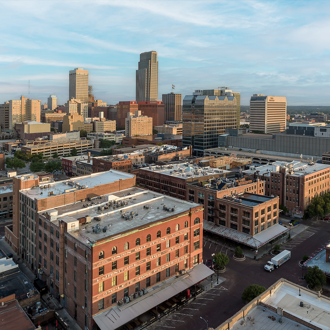 Aerial view of Omaha downtown skyline featuring historic Old Market district and modern high-rise buildings under a blue sky.