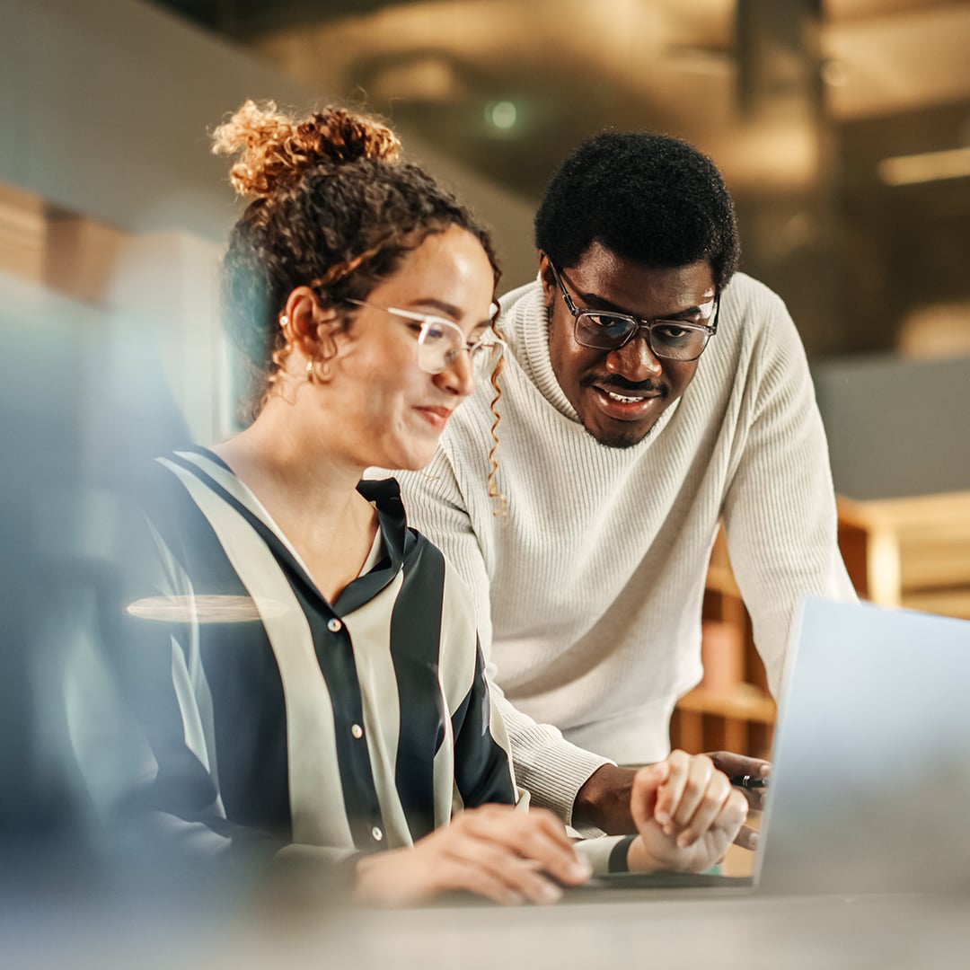 Two colleagues reviewing data together on a laptop, illustrating how CBRE's Next Action Engine surfaces cross-system portfolio insights to drive the next wave of occupancy savings