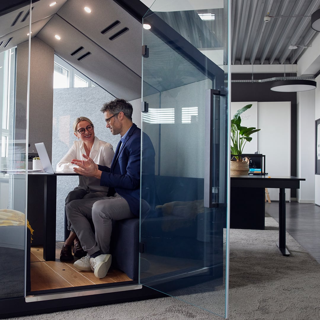 Two colleagues collaborating inside a modern glass office pod