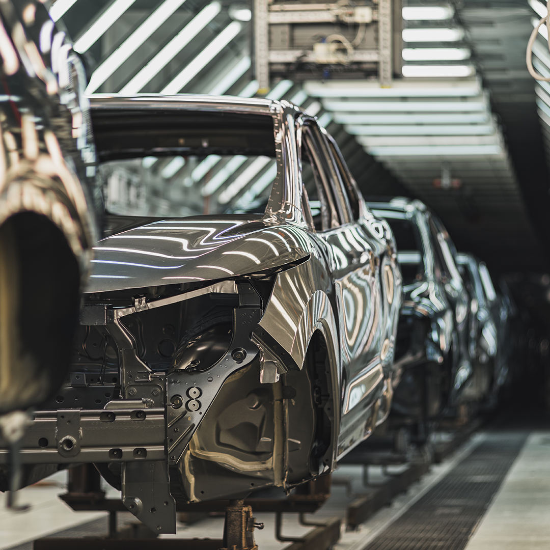 Row of metallic car bodies on an automotive factory assembly line under bright lights