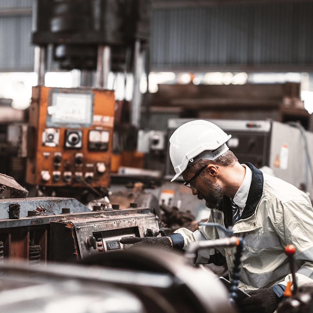 Worker in a hard hat and safety glasses operates industrial machinery inside a factory