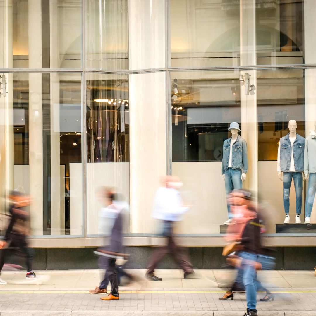 A long exposure shot captures blurry pedestrians walking past a shop window displaying mannequins dressed in denim outfits.