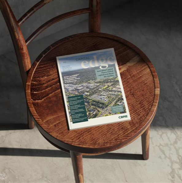 A CBRE "Capital Edge" magazine rests on a rustic wooden chair in a sun-drenched, minimalist setting.