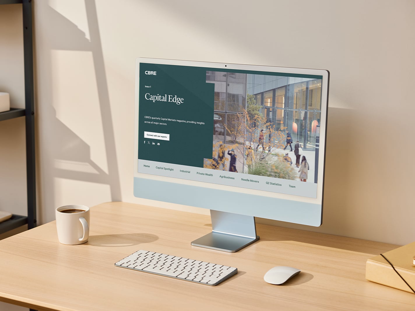 Desktop computer displaying the CBRE Capital Edge website on a tidy office desk with a keyboard, mouse, and coffee mug. 