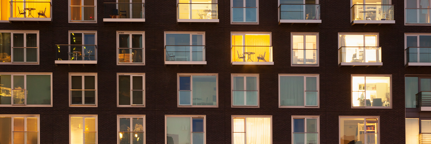 Apartment building facade with illuminated windows and balconies at dusk.