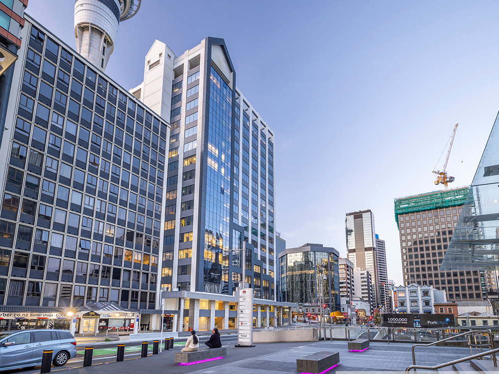 Modern glass-clad office tower within a dense city centre streetscape, surrounded by high-rise buildings and public plaza areas.