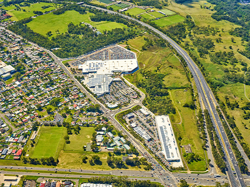 Aerial view of a large shopping centre surrounded by residential neighbourhoods, open green space and major transport corridors.