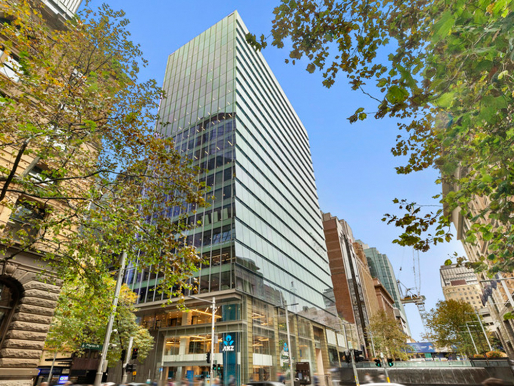 Contemporary commercial office building with a glazed façade, framed by street trees along a busy urban boulevard.