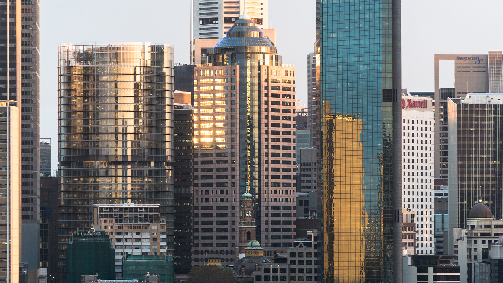 Sydney CBD skyline featuring modern office towers with reflective glass facades surrounding a historic clock tower at golden hour.