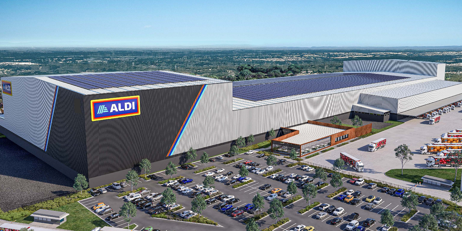 Large ALDI-branded distribution warehouse with solar panels on the roof, a busy parking lot filled with cars, and delivery trucks loading and unloading goods near the facility.