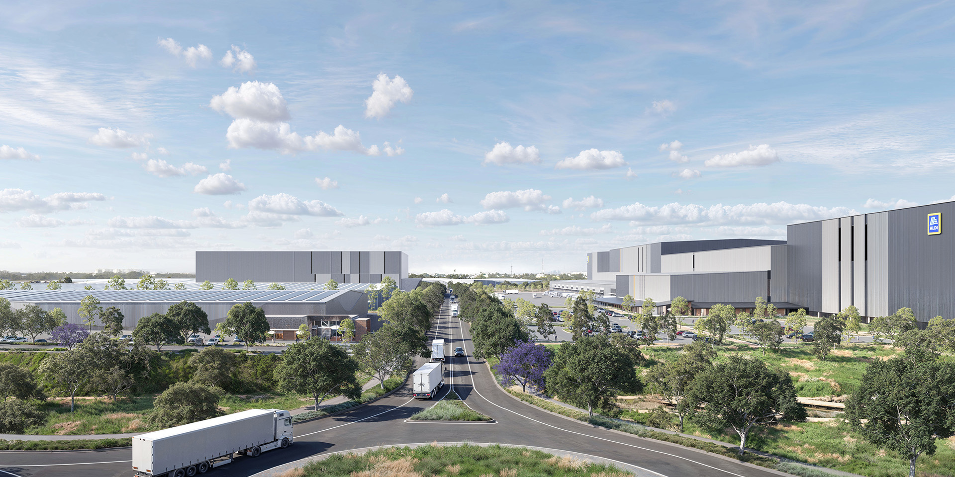 Modern logistics and distribution center with large warehouse buildings, ALDI branding, and solar panels, viewed from above a landscaped roundabout with multiple semi-trucks traveling along a tree-lined central road under a partly cloudy sky.