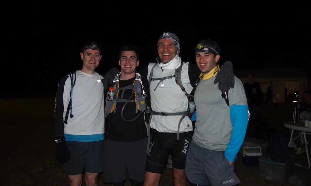 A group of four participants wearing running gear and headlamps pose together at a nighttime endurance event, with James King standing second from the left.