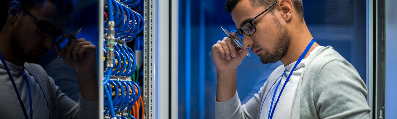 Side view  portrait of young man standing by server cabinet while working with supercomputer in data center and holding clipboard