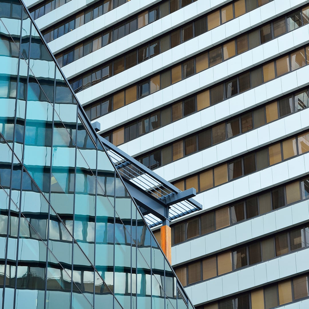 A modern building features a blue glass facade on the left, angled against a white and brown striped building with many horizontal windows on the right.
